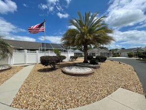 A residential area with houses, a white picket fence, a palm tree, and an American flag.