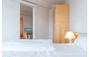 Une chambre d’hôtel avec un lit, une table de chevet avec une lampe, une armoire en bois et une vue sur un paysage visible par une porte ouverte.