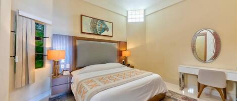 A hotel room with a bed, bedside lamps, a desk, a chair, a mirror, and a window with curtains.
