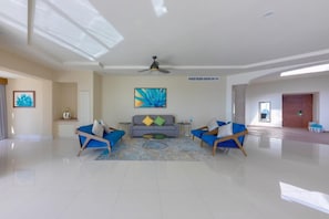 Ein großzügiges Wohnzimmer im modernen Design, mit einer Sofagarnitur, einem Couchtisch und einem Deckenventilator.