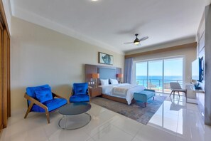 A hotel room with a bed, two blue armchairs, a small table, a desk, and a large window with a view of the ocean. - Villa del Palmar - Penthouse - 4BR/4BA - 6,600+ Sq.Ft! (Cabo San Lucas)