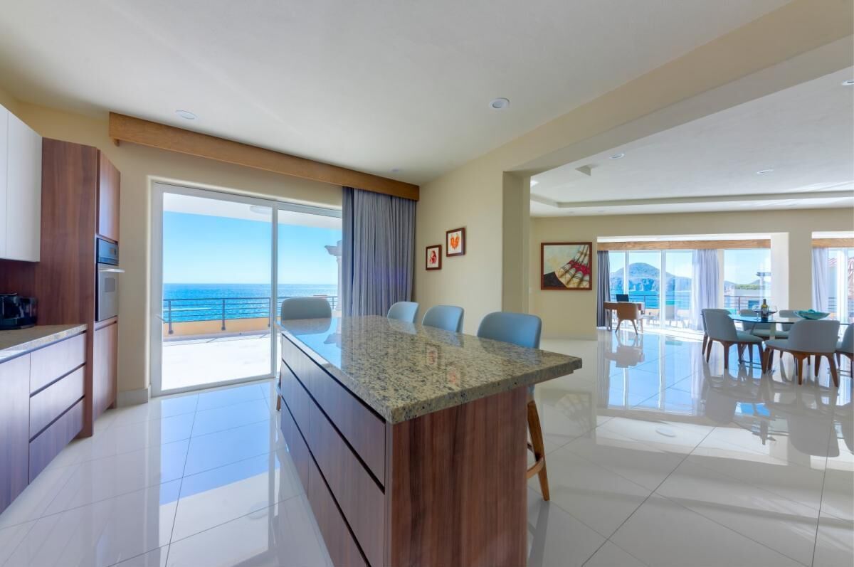 Een moderne keuken met een groot eiland, een eethoek met uitzicht op de oceaan, en een ruime woonkamer met een balkon.