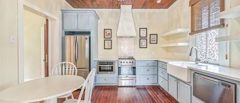 A kitchen with wooden flooring, a chandelier, a stove, and a sink.