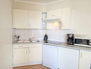 A compact kitchen with white cabinets, a dishwasher, a coffee maker, and a microwave. - Ferienwohnung mit Hund in Sellin (Sellin)