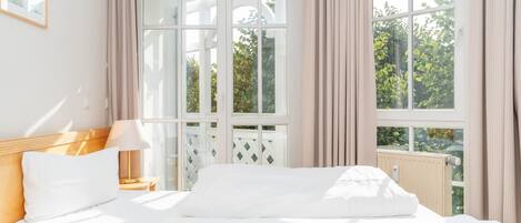 A hotel room with a bed, a nightstand, a lamp, and a window with curtains.