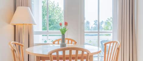 Un comedor con una mesa redonda, cuatro sillas de madera, un florero con flores y una lámpara.
