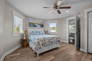 Ein Schlafzimmer mit einem Bett, einem Deckenventilator, einem Gemälde und einem durch eine offene Tür einsehbaren Badezimmer.