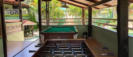 A foosball table in a room with a view of a pool and greenery outside.