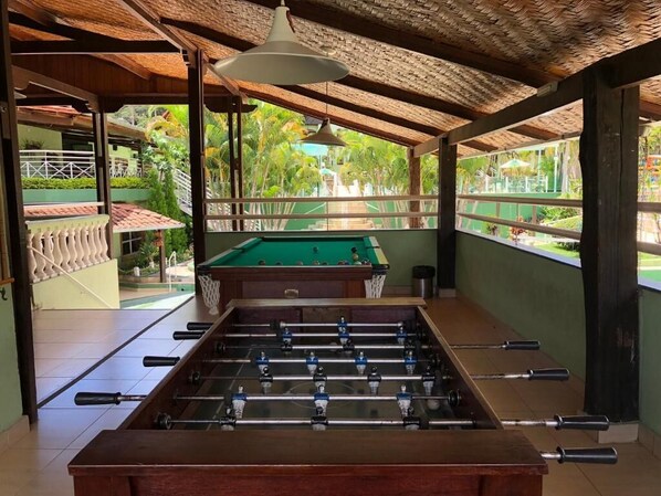A foosball table in a room with a view of a pool and greenery outside. - Gran minas Hotel (Vespasiano)