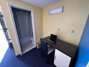 A small room with a desk, chair, and a door leading to a bathroom. - WELCOME INN (North Kingstown)