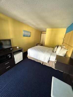 Una habitación de hotel con cama, escritorio, silla, televisor y una mesita.
