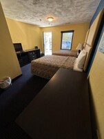 Una habitación de hotel con cama, escritorio, silla, televisor y ventana.