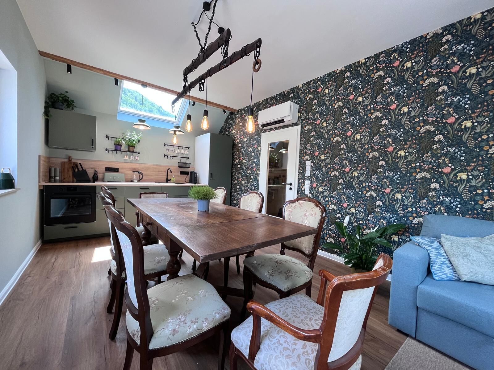 Eine moderne Küche mit Essbereich, einem blauen Sofa und blumigem Wandpapier.
