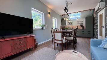 Ein Wohnzimmer mit Fernseher, Esstisch, Stühlen und einem blauen Sofa.
