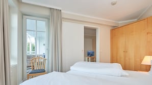 Hotellihuone, jossa on kaksi sänkyä, puinen vaatekaappi, tuoli, pieni pöytä lampun kanssa ja televisio.
