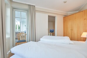 A hotel room with two beds, a wooden wardrobe, a chair, a small table with a lamp, and a television. - In Attraktiver Lage des Ostseebades Sellin (Sellin)