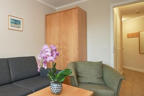A living room with a sofa, a green armchair, a wooden wardrobe, and a table with an orchid plant. - In Attraktiver Lage des Ostseebades Sellin (Sellin)