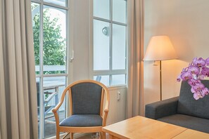 A room with a wooden chair, a grey sofa, a wooden table, a window with curtains, and a lamp with purple flowers. - In Attraktiver Lage des Ostseebades Sellin (Sellin)