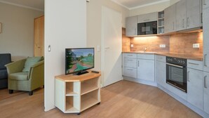 Moderni keittiö, jossa on harmaat kaapit, sisäänrakennettu uuni ja televisio puukorokkeella.