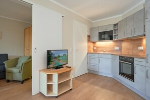 A modern kitchen with grey cabinets, a built-in oven, and a TV on a wooden stand. - In Attraktiver Lage des Ostseebades Sellin (Sellin)