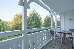 Un espace extérieur abrité, doté d’une table et de chaises, de rampes blanches et offrant une vue sur les arbres.
