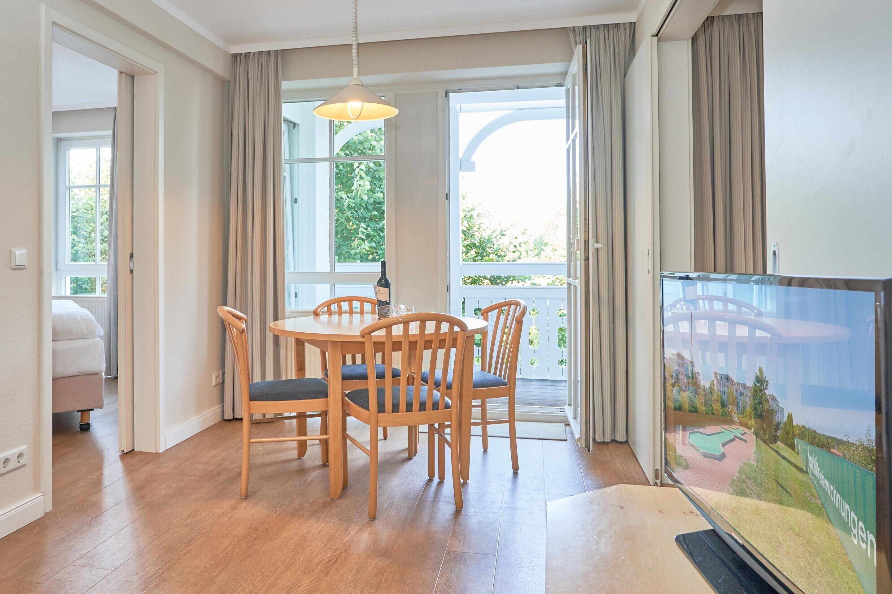 En matplats med ett bord och stolar, en tv och utsikt över en byggnad och grönska utanför.