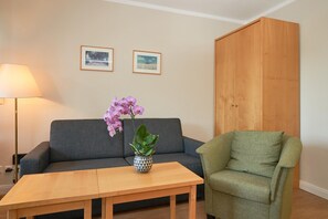 A living room with a sofa, a green armchair, a wooden coffee table, a lamp, and two framed pictures on the wall. - In Attraktiver Lage des Ostseebades Sellin (Sellin)