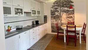 Uma cozinha moderna com armários brancos, uma cafeteira e uma área de refeições com uma cadeira vermelha e uma mesa.