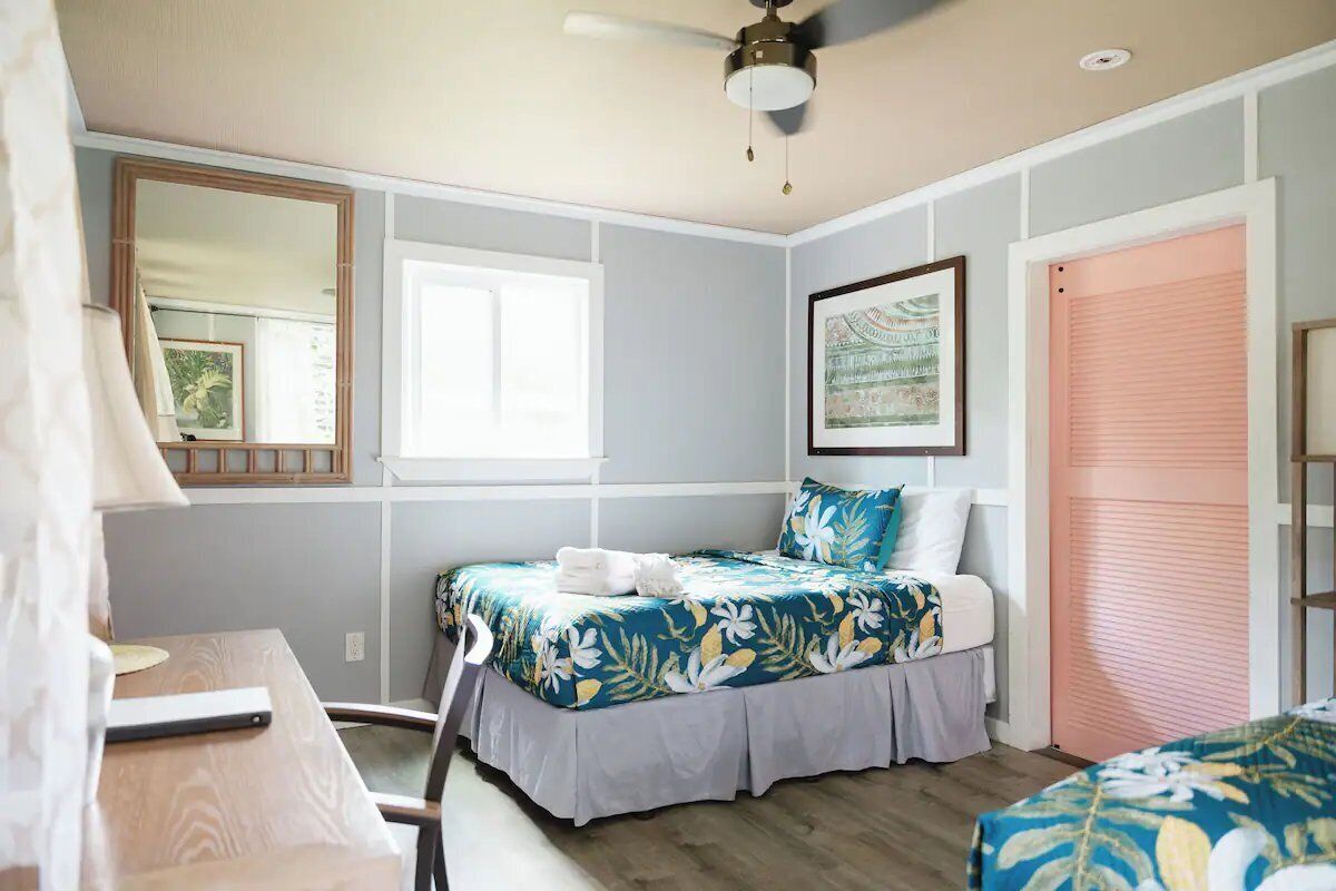 Une chambre à coucher comprenant un lit, un bureau, une chaise, un ventilateur de plafond, une fenêtre et une porte.