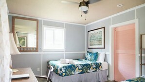 A bedroom with a bed, a desk, a chair, a ceiling fan, a window, and a door.