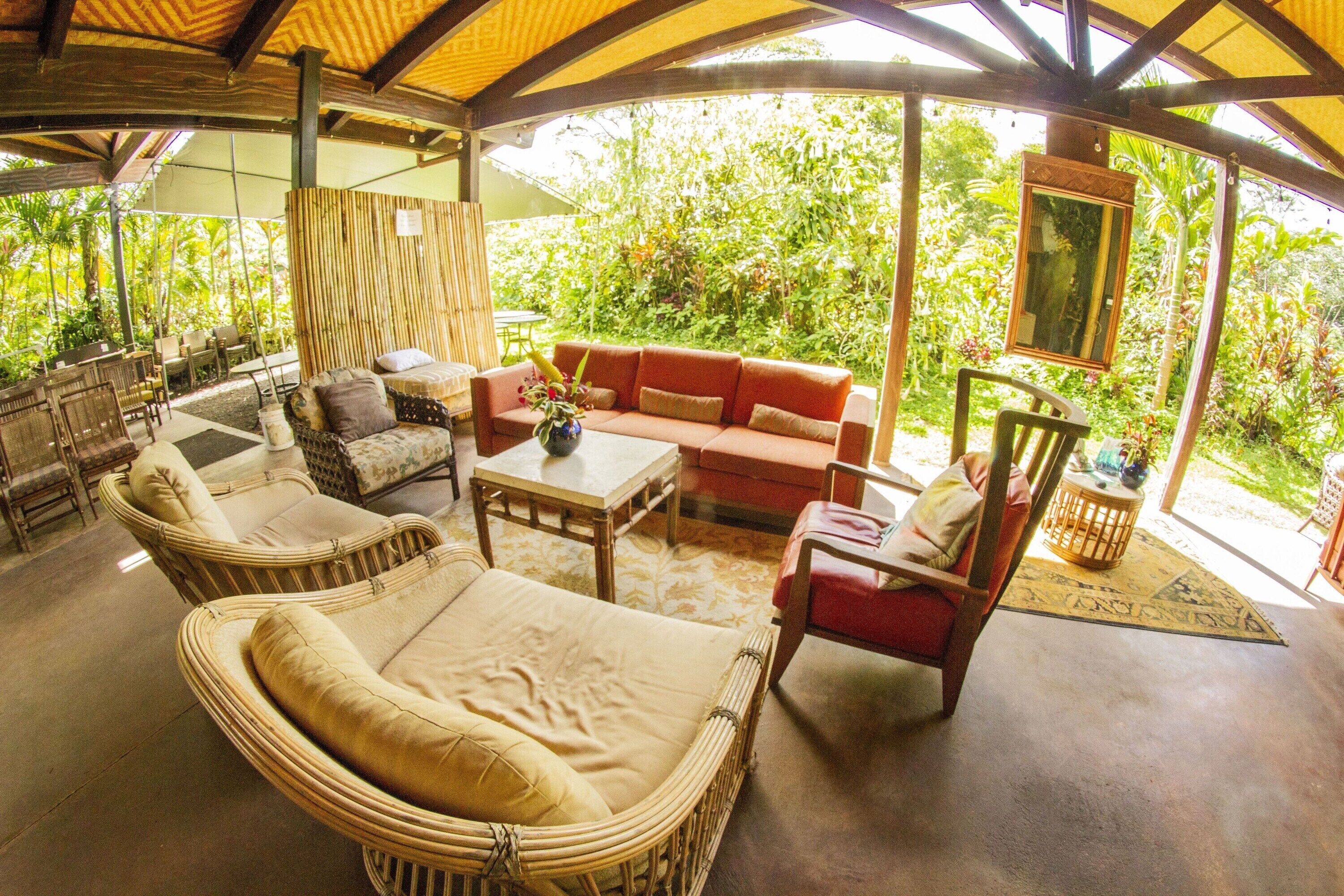 An open-air lounge with wicker furniture, a red sofa, and a table with a vase.