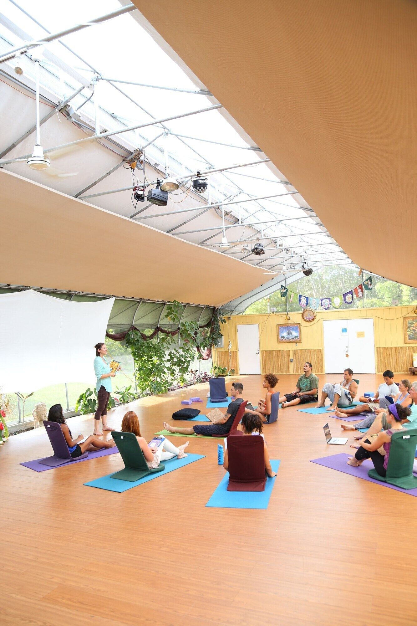 Una clase de yoga en un espacio amplio con techo alto, ventanas grandes y suelo de madera.