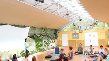 Una clase de yoga en un espacio amplio con techo alto, ventanas grandes y suelo de madera.