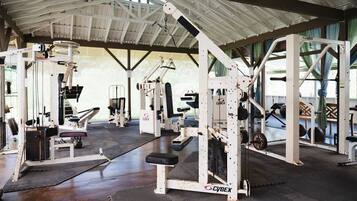 A gym with various exercise equipment, including weight machines and free weights, under a covered roof.