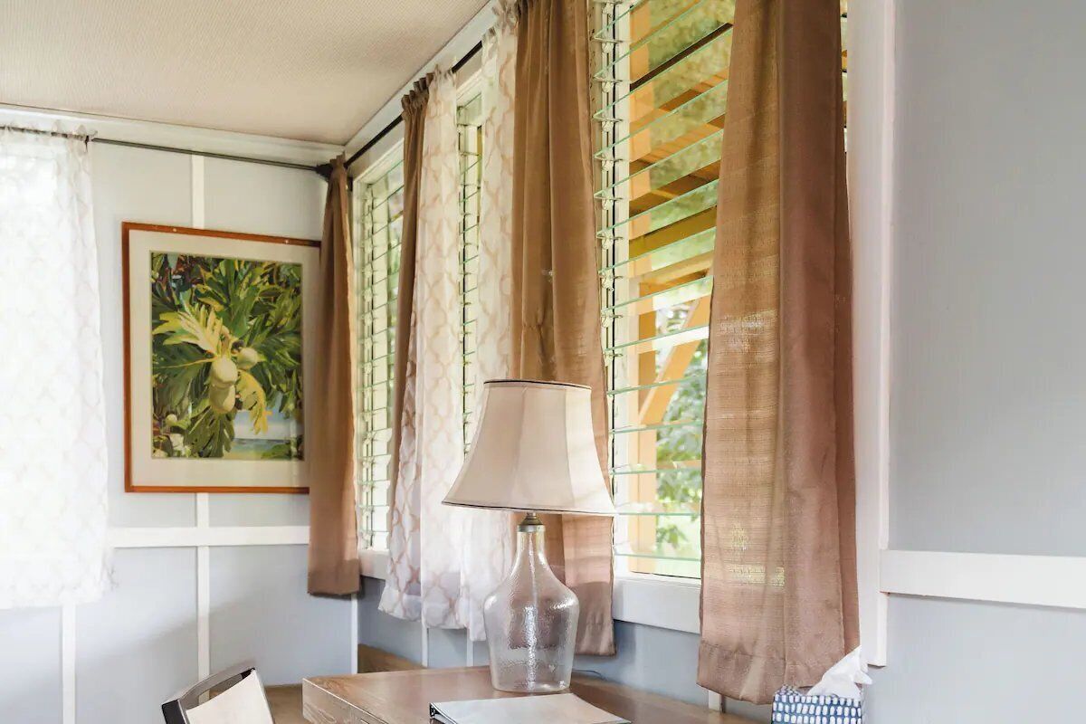 A room with a table, a lamp, a framed picture, and window blinds.