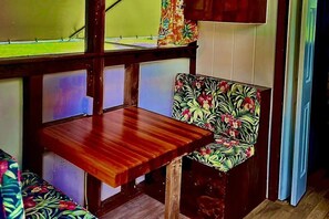 Un banco de madera con un cojín floral, una ventana con cortina y una mesa de madera.