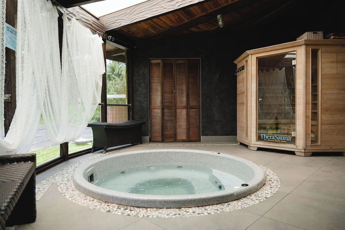 Wellnessbereich mit Whirlpool, Holzbiosauna und Fenster mit transparenten Vorhängen.