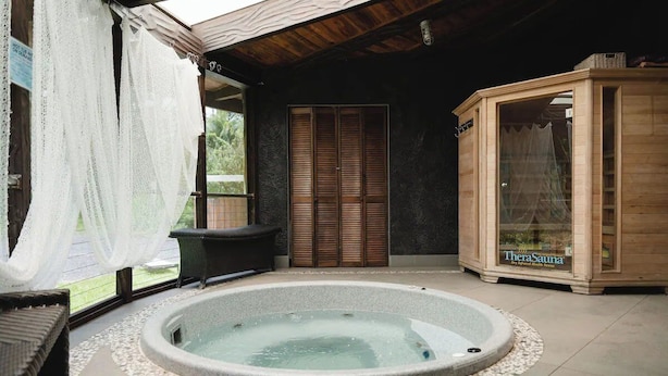 A spa area with a hot tub, wooden sauna, and a window with sheer curtains.