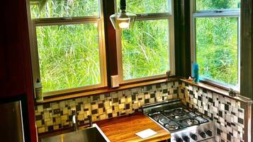 A kitchen with a tiled backsplash, a gas stove, a sink, and large windows overlooking greenery.