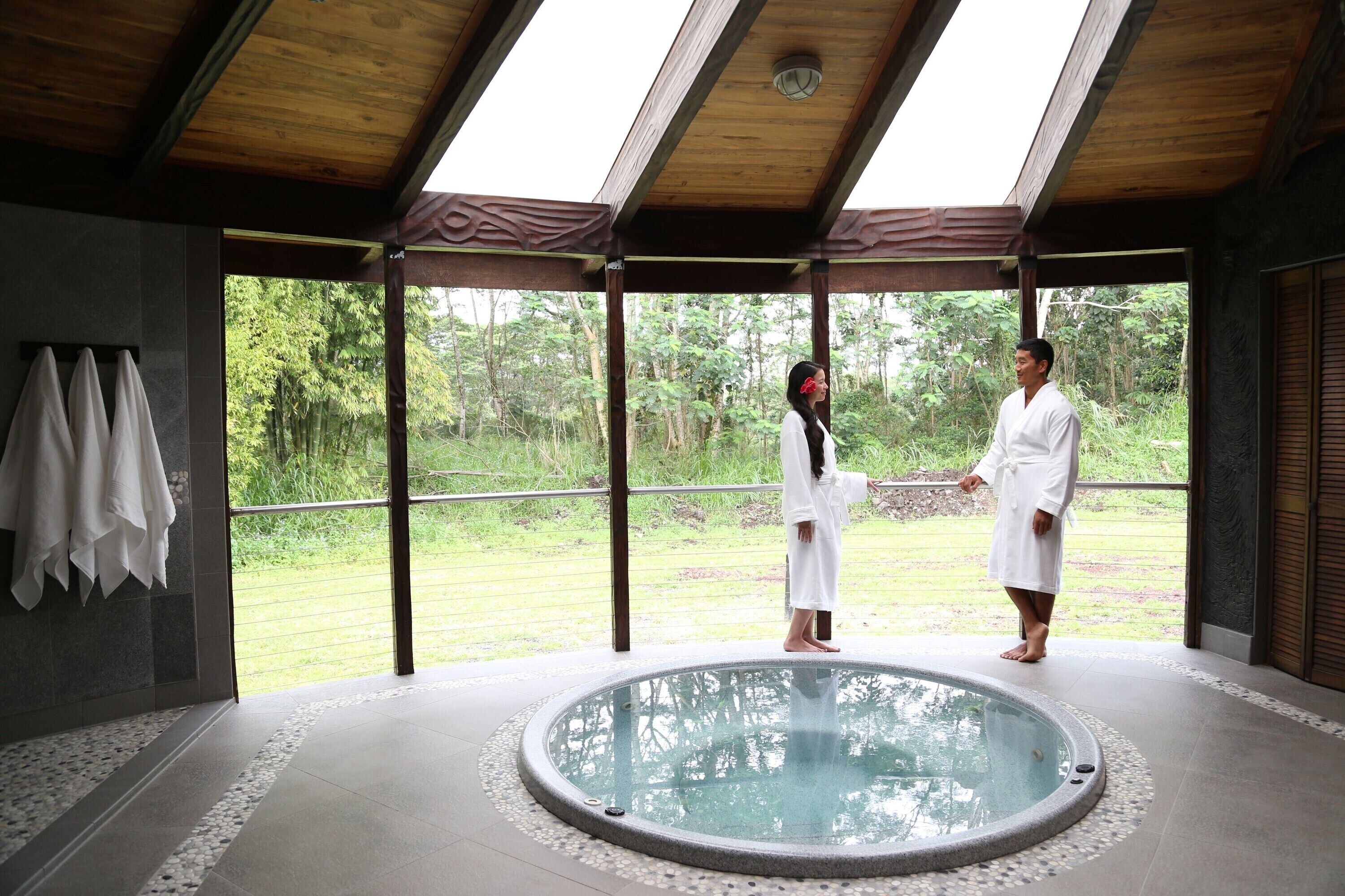 A spa area with a hot tub, wooden ceiling, and a view of greenery.