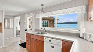 Une cuisine avec vue sur la mer, un lave-vaisselle et des meubles de rangement en bois.