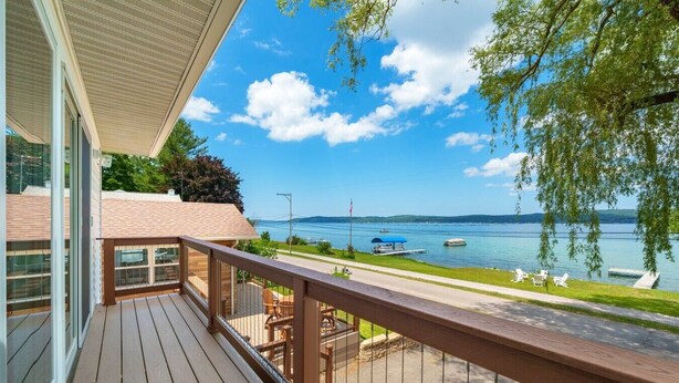 Une terrasse en bois avec une rambarde, donnant sur un lac où l’on peut voir des bateaux et un ciel dégagé.