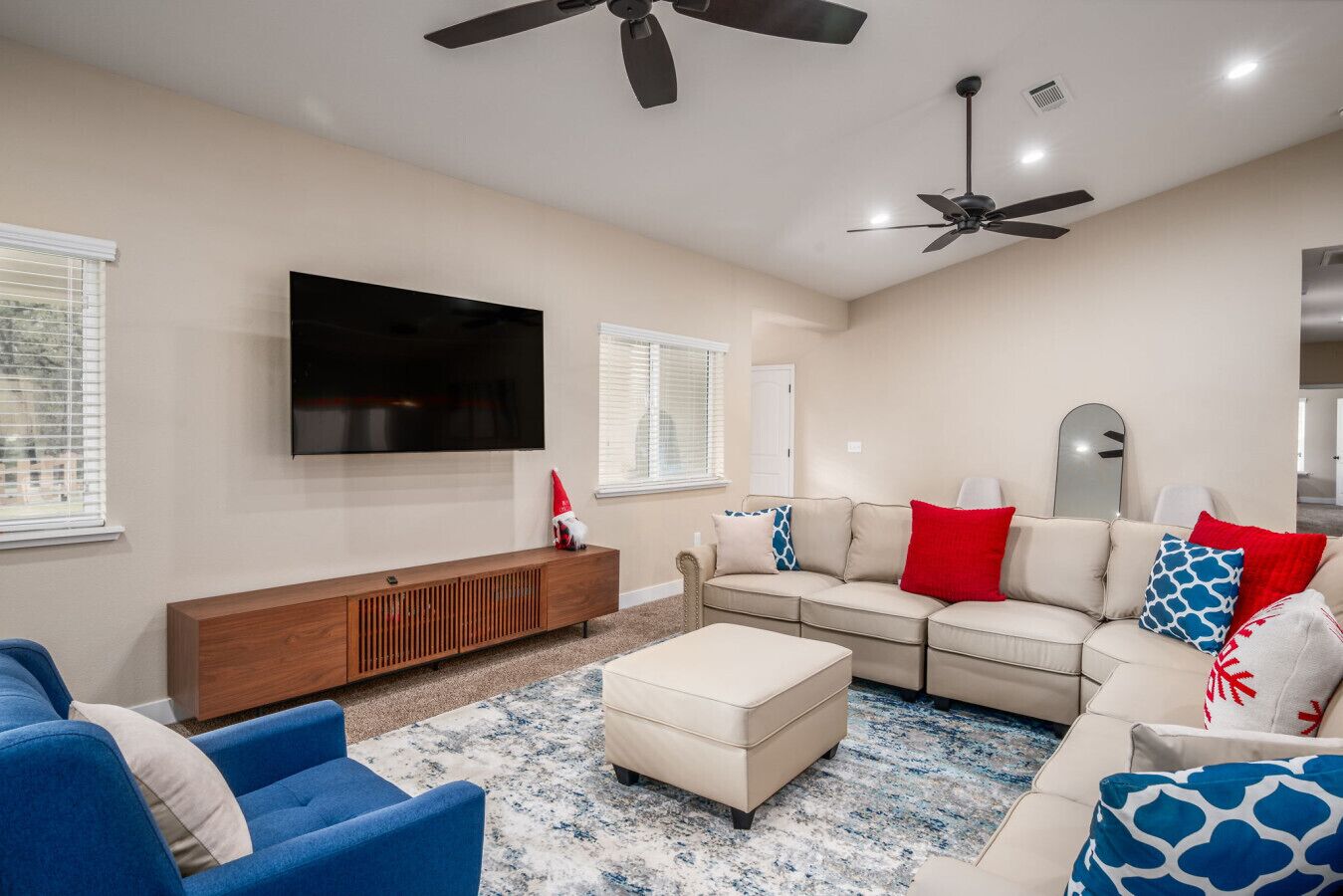 A modern living room with a flat-screen TV, two ceiling fans, a sectional sofa, a wooden console, and a patterned rug.