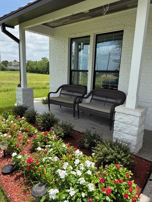 A covered porch with two wicker chairs, a brick wall, and a garden with flowers. - Spacious 4-bedroom house in nice Katy with cool vibes (Katy)