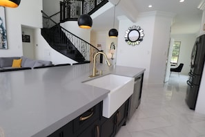 Une cuisine moderne dotée d’un îlot central, de meubles de rangement noirs et blancs, d’un réfrigérateur en acier inoxydable et d’un escalier avec des rampes noires.