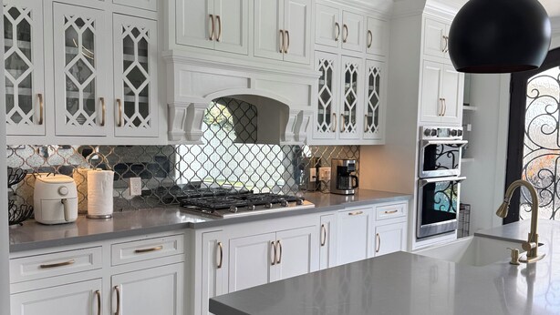 Une cuisine moderne avec des meubles blancs, un luminaire suspendu noir et un dosseret carrelé.