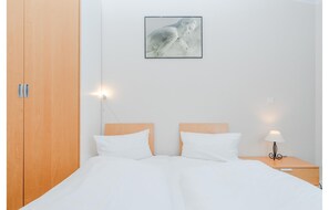 Ein Schlafzimmer mit Holzschrank, einem Bett mit weißer Bettwäsche, einem Nachttisch mit Lampe und einem gerahmten Bild an der Wand.