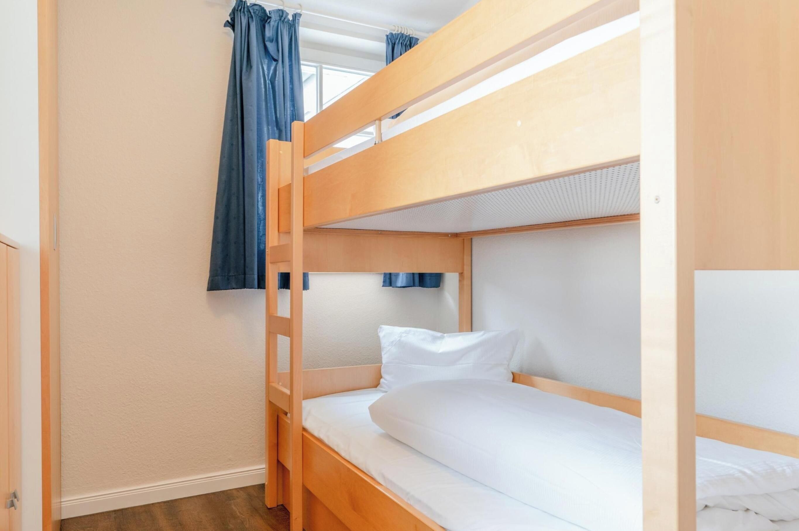 Habitación con literas, una escalera, ropa de cama blanca y cortinas azules.
