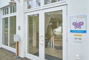 A white building with a glass door, a butterfly logo sign, and a number sign. - Ferienwohnung im 3.og mit Balkon in Sellin (Sellin)