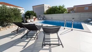 En swimmingpool med liggestole, et bord og en lille træterrasse.
